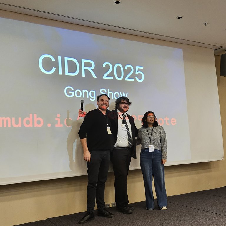 Hannes Mühleisen at CIDR 2025, standing next to 2 people, posing as winner of the Gong show